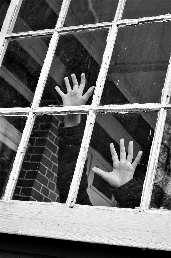Schwarz-weiss-Foto: Handflächen an Gitterfenster