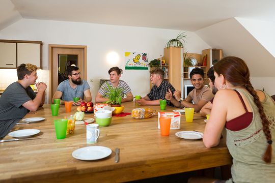 Fünf jugendlichen Bewohner und zwei junge Mitarbeiter im Betreuten Wohnen in Woltersdorf unterhalten sich angeregt am großen, reich gedeckten Frühstückstisch.